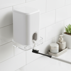 Wall mounted automatic toothpaste dispenser with toothbrush holder in clean bathroom